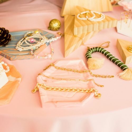 Chic collection of stylish jewelry displayed on a pink surface with geometric accents.